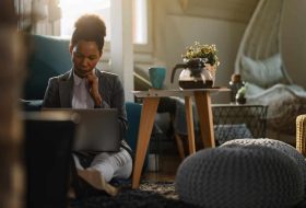 thoughtful-african-american-businesswoman-working-computer-while-siting-floor-home-office